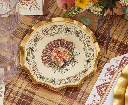 The Sophistiplate LLC Turkey & Gourds Table Setting Bundle features a decorative plate with a detailed turkey illustration at the center and a floral border, elegantly arranged on a plaid tablecloth alongside glassware and cutlery—a perfect example of designer disposable plates that blend festive style with convenience for any holiday gathering.